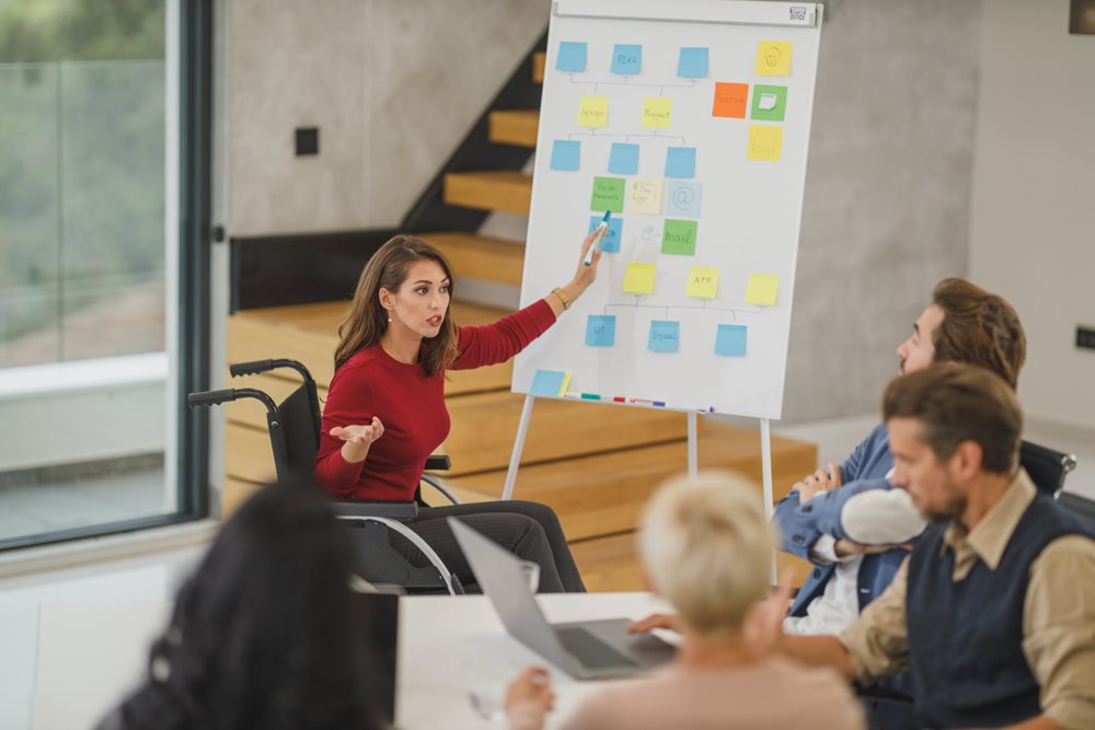Woman presenting on whiteboard with colorful post it notes.