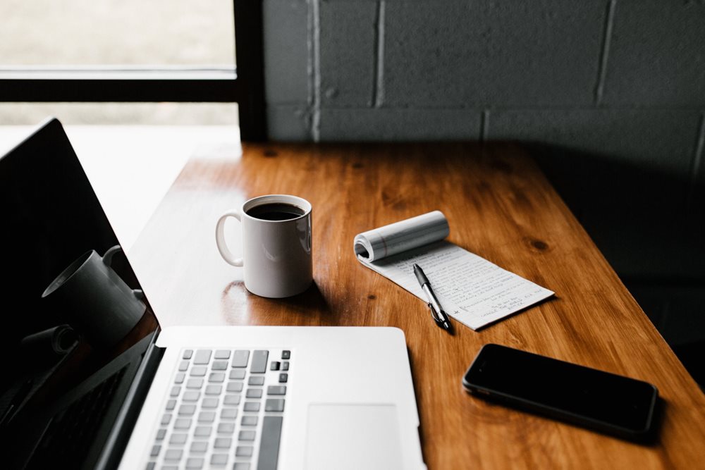 Laptop, notebloc, smartphone and cup of coffee, on a wooden desk.