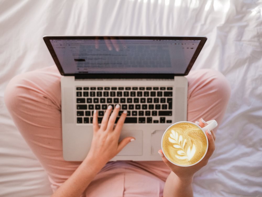 Woman working on laptop, cappuccino in hand.