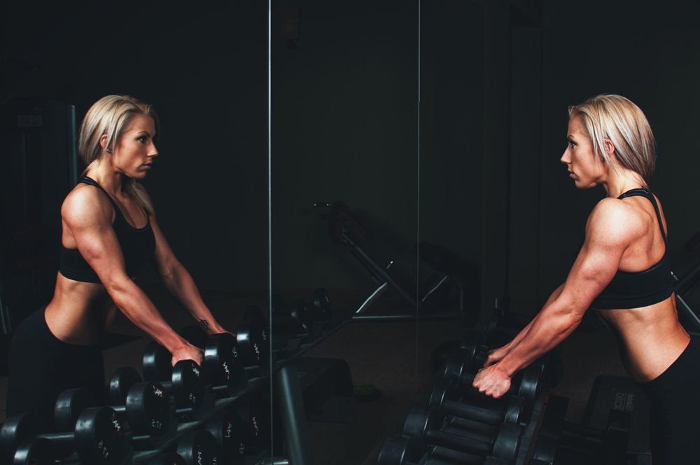 Woman holding dumbbells, looking in the mirror.