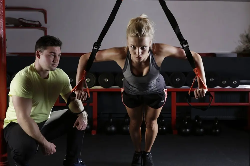 Male personal trainer helping woman do cable push ups.
