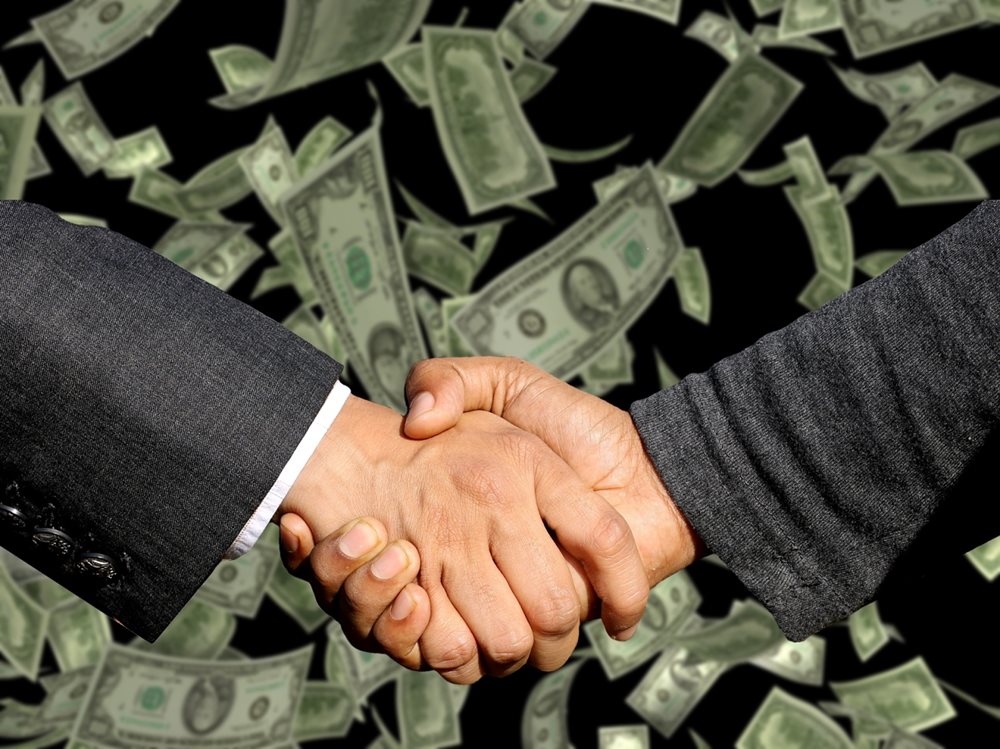 Two men shaking hands with money in the background.